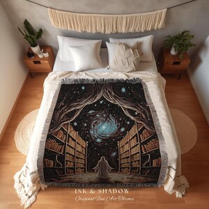 May include: A woven throw blanket depicting a celestial library scene with a swirling galaxy and a figure in a white robe. The design includes bookshelves, trees, and the text "INK & SHADOW Original Fine Art Throws."