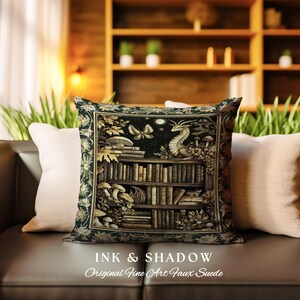 May include: A decorative pillow with a dark green background featuring a bookshelf filled with books, a dragon, and butterflies. The text "Ink & Shadow Original Fine Art Faux Suede" is printed below the image.