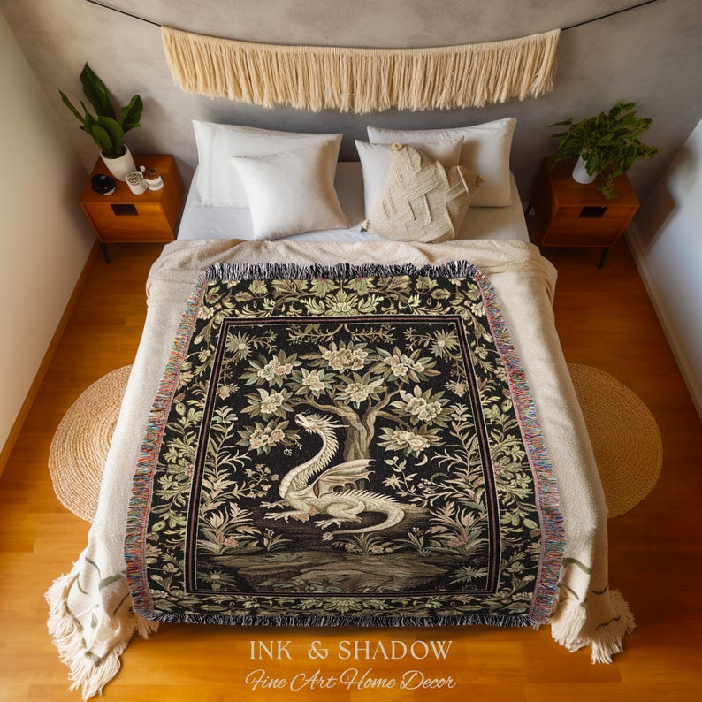 May include: A woven throw blanket featuring a black background with a central white dragon illustration surrounded by detailed floral and tree motifs. The blanket has a fringed edge and displays the text INK & SHADOW Fine Art Home Decor.