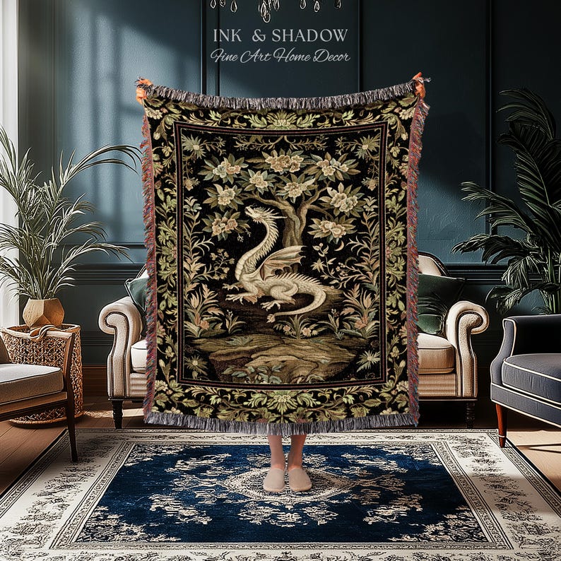May include: A woven throw blanket featuring a central illustration of a white dragon perched on a rock beneath a flowering tree, set against a black background with a decorative floral border and fringed edges, displaying the text Ink & Shadow.