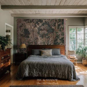 May include: A bedroom scene featuring a bed with a gray comforter and pillows, a wooden headboard, and a tapestry depicting a forest scene. The room includes a wooden dresser, a nightstand with a lamp, and a window with natural light.