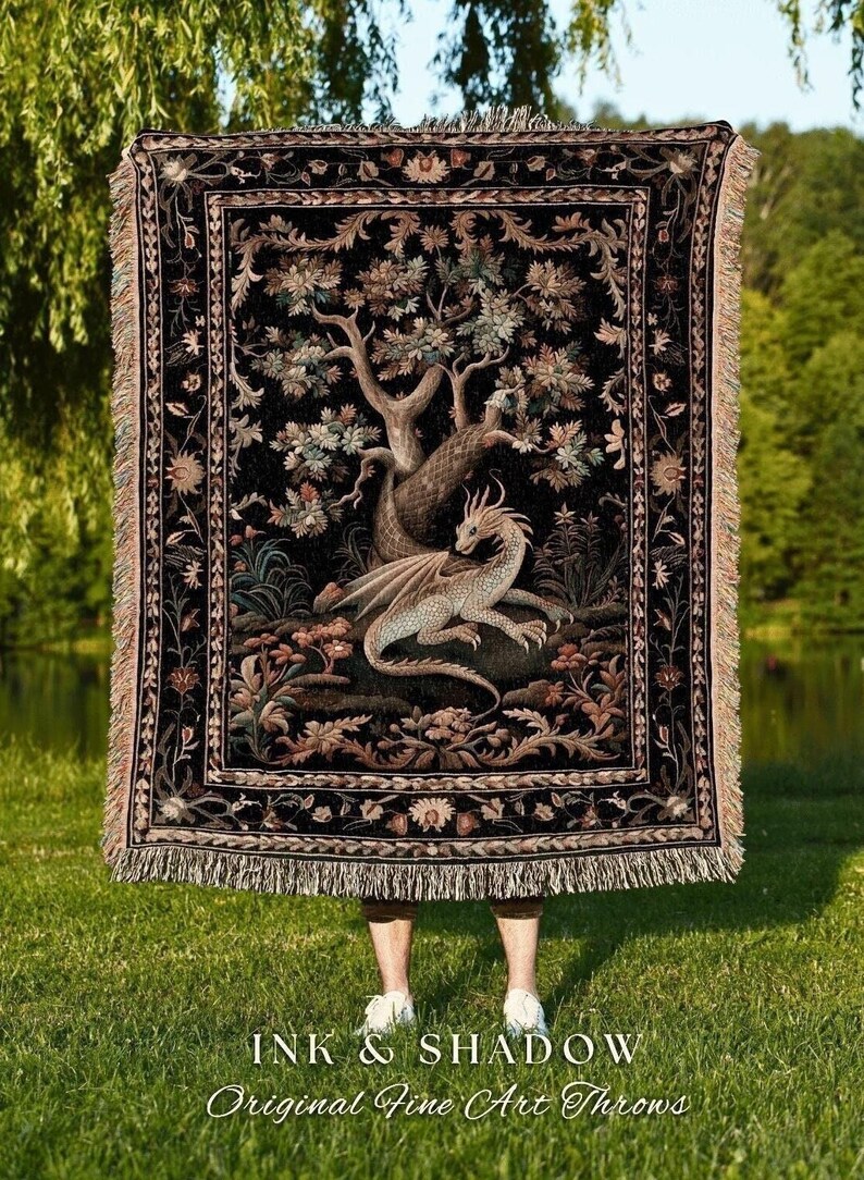 May include: A black throw blanket with a detailed illustration of a dragon resting beneath a tree. The blanket has a fringed edge and the text "INK & SHADOW Original Fine Art Throws" at the bottom.