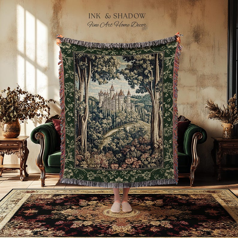 May include: A woven tapestry throw blanket featuring a detailed landscape scene of a castle nestled among trees. The blanket has a dark green border with floral patterns and fringed edges. Text at the top reads INK & SHADOW Fine Art Home Decor.