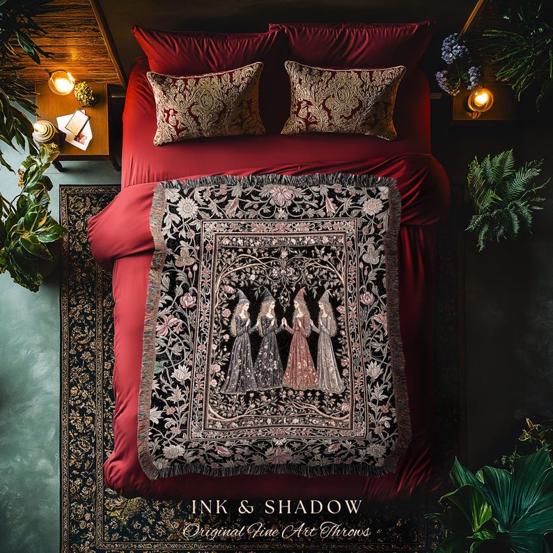 May include: A woven throw blanket featuring a central illustration of four figures in pointed hats standing in a circle, surrounded by a floral border on a black background. The text "INK & SHADOW Original Fine Art Throws" is printed at the bottom.