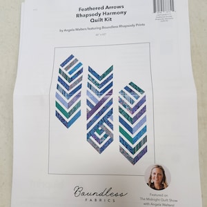 May include: A quilt kit featuring a pattern of three blue, purple, and green feathered arrows. The kit is called "Feathered Arrows Rhapsody Harmony Quilt Kit" and is by Angela Walters featuring Boundless Rhapsody Prints. The kit is 46 inches by 60 inches.