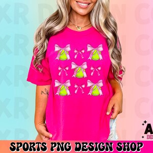 May include: A pink t-shirt with a design of pink bows and yellow tennis balls. The text "SPORTS PNG DESIGN SHOP" is at the bottom of the image.