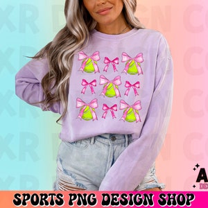 May include: A lavender sweatshirt with a graphic design of pink bows and yellow tennis balls. The graphic design is repeated across the front of the sweatshirt.