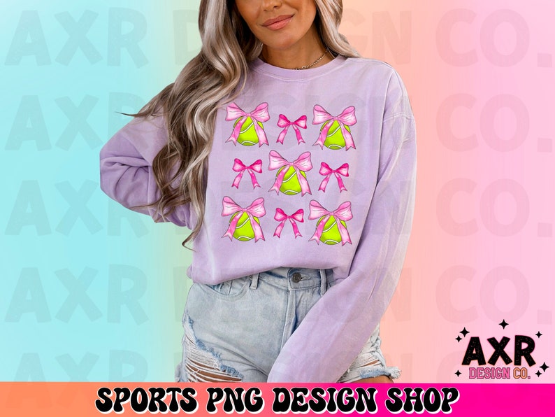May include: A lavender sweatshirt with a graphic design of pink bows and yellow tennis balls. The graphic design is repeated across the front of the sweatshirt.