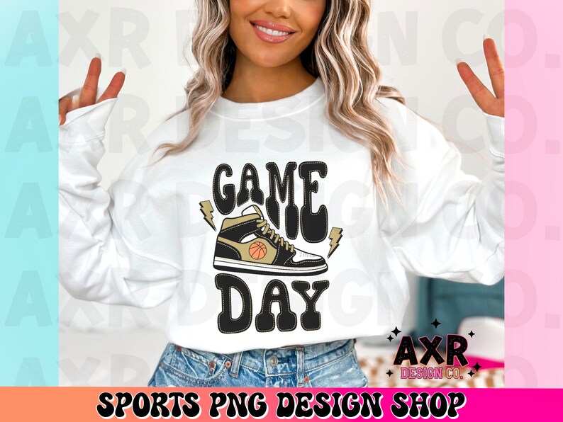 May include: White sweatshirt with the text "GAME DAY" in black and gold lettering. A black and gold basketball shoe with a basketball graphic is above the text.