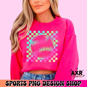May include: A bright pink sweatshirt featuring a baseball graphic with a checkered background in shades of green, blue, and pink. The baseball design is outlined in a gradient of pink and green. The text "SPORTS PNG DESIGN SHOP" is at the bottom.