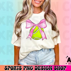 May include: A white t-shirt with a pink bow and a green tennis ball design. The design features a pink bow with glitter accents and a green tennis ball with white stitching.
