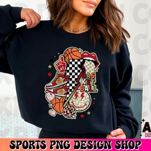K&ouml;nnte beinhalten: Schwarzes Sweatshirt mit einem Basketball-Motiv. Das Design umfasst Basketb&auml;lle, einen Turnschuh, Lippen, einen Blitz und die Worte "Basketball". Das Design enth&auml;lt auch ein Schachbrettmuster und Sterne.