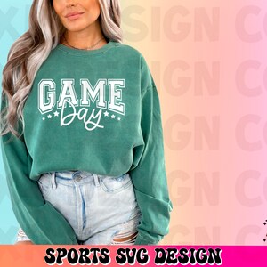 May include: A green sweatshirt with the text "GAME Day" in white lettering. The sweatshirt is being worn by a person with long brown hair.