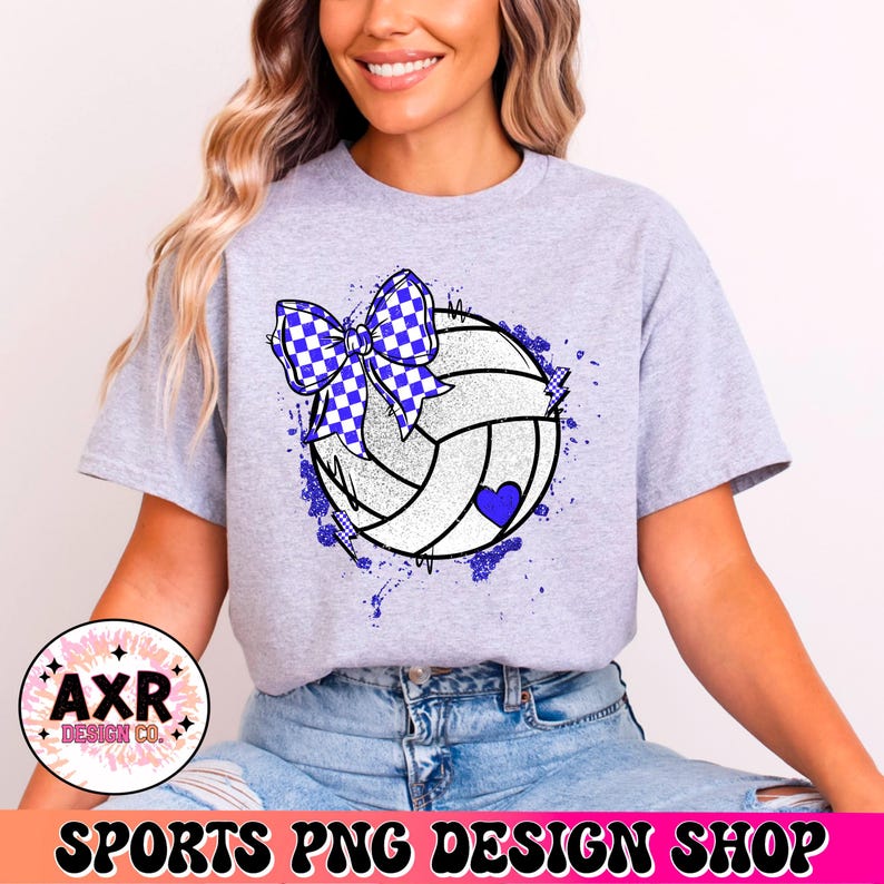 Op de afbeelding: Een grijs T-shirt met een witte volleybal met een blauw-wit geblokt strikje erop. De volleybal heeft een blauw hartje en is omringd door blauwe verfspatten.