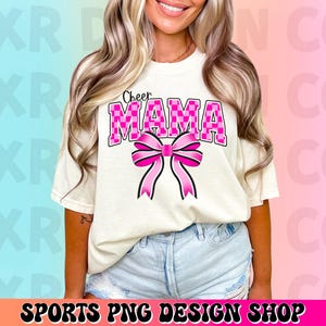 May include: A white t-shirt with the text "Cheer Mama" in pink and black checkered letters. A pink bow with a checkered pattern is below the text.