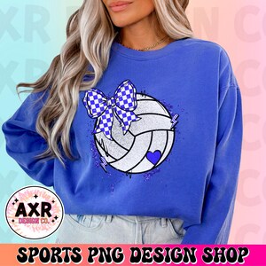 Op de afbeelding: Een blauw sweatshirt met een witte volleybal met een blauwe strik erop. De volleybal heeft een blauw hart en is omringd door glitter.