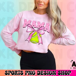 May include: Pink long-sleeved shirt with the word "MAMA" in a white outline and a pink bow with a green tennis ball in the center.
