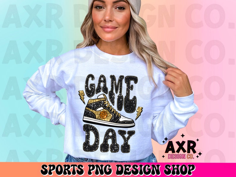 May include: White sweatshirt with the text "GAME DAY" in black glitter letters and a black and gold basketball shoe graphic. The text "AXR DESIGN CO." is in the bottom right corner.
