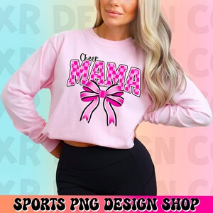 May include: Pink long-sleeved shirt with the text "Cheer Mama" in pink and white checkered letters with a pink bow.