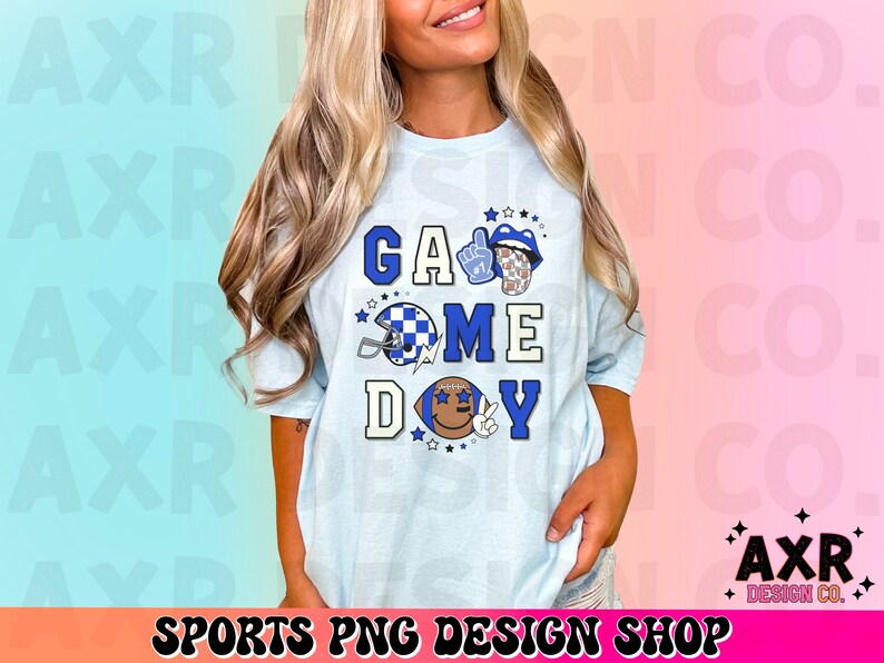 May include: A light blue t-shirt with the text "Game Day" in blue and white letters. The shirt features a football helmet, a hand giving a thumbs up, and a tongue sticking out.