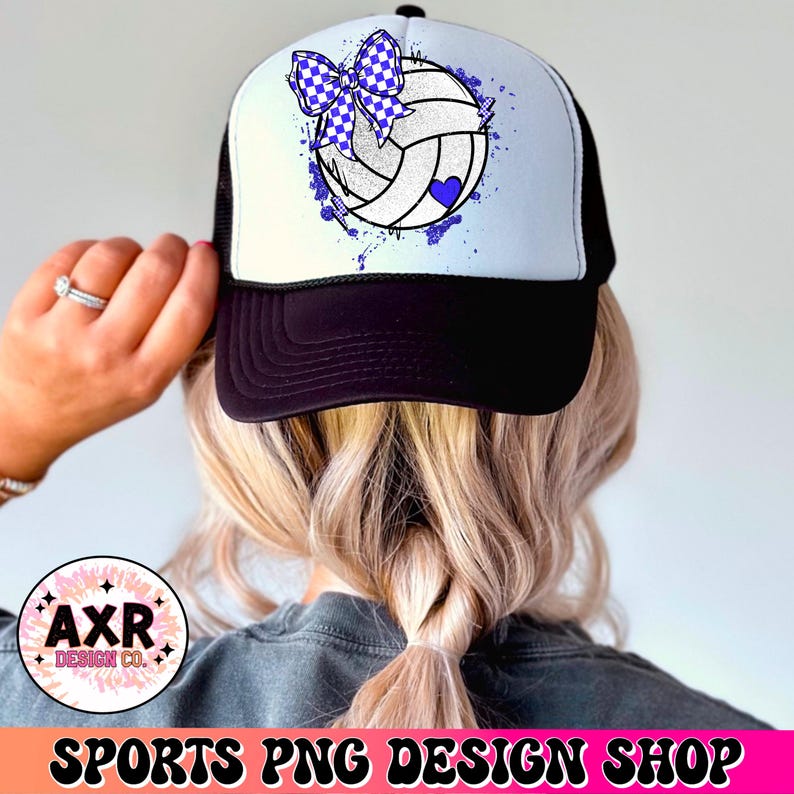 Op de afbeelding: Een witte en blauwe volleybal met een blauwe strik erop, met een wit hart in het midden van de volleybal. De volleybal zit op een witte en blauwe truckercap met een zwart mesh achterkant.