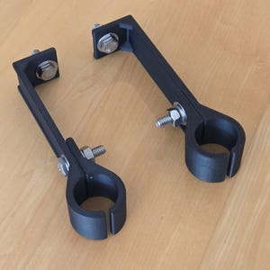 May include: Two black plastic brackets with a circular clamp on one end and a rectangular mounting plate on the other. The brackets are secured with silver screws.