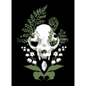 May include: A white cat skull with a green fern and lily of the valley floral arrangement. The skull is centered in the image with the flowers surrounding it.