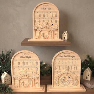May include: Three arched wooden plaques featuring laser-engraved nativity scenes and musical notation. Two plaques display the text Silent Night, while one displays Away In A Manger. Each piece includes a stable, figures, and palm trees.