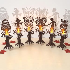 May include: A set of six dark brown wooden candle holders, each featuring a unique cutout design including a skull, scarecrow, butterfly skull, haunted house, zombie, and cauldron. Each holder supports a small tea light candle.