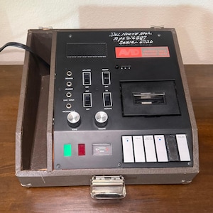 May include: A brown portable Avid cassette tape recorder with a black control panel featuring volume and tone knobs, various input jacks, a cassette compartment, and mechanical playback buttons. The unit has handwritten text reading Del Norte High.