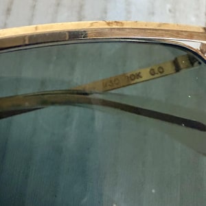 May include: Gold-tone metal sunglasses featuring dark green tinted lenses. The interior bridge of the frame is clearly engraved with the text M30 10K G.O. The design includes a thin, polished gold-colored metal brow bar and matching frame rims.