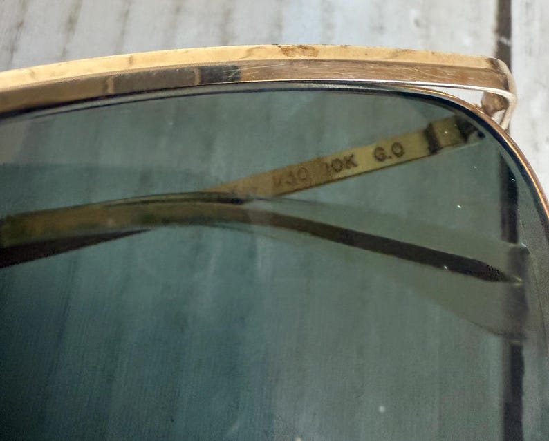 May include: Gold-tone metal sunglasses featuring dark green tinted lenses. The interior bridge of the frame is clearly engraved with the text M30 10K G.O. The design includes a thin, polished gold-colored metal brow bar and matching frame rims.