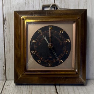 May include: A square, vintage barometer with a dark face and gold-tone hands, set in a wooden frame. The face displays numbers and the words "REGEN" and "SCHON". A metal loop is attached at the top for hanging.