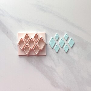 Pu&ograve; includere: Un tagliapasta rosa in argilla polimerica a forma di diamante, accanto a diversi orecchini a forma di diamante azzurro. Gli orecchini hanno una superficie strutturata e un piccolo foro nella parte superiore.