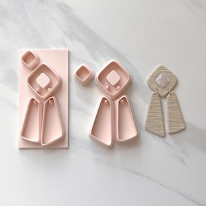 May include: A collection of pink polymer clay cutters in various geometric shapes. The set includes diamond, square, and trapezoid shapes, perfect for crafting earrings and other jewelry. One pair of earrings is also shown, featuring a textured, neutral-toned design.