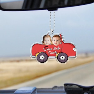 May include: Red car shaped rearview mirror charm with two children's faces in the windows. The car has yellow wheels and the text "Drive Safe Daddy" is printed on the car.