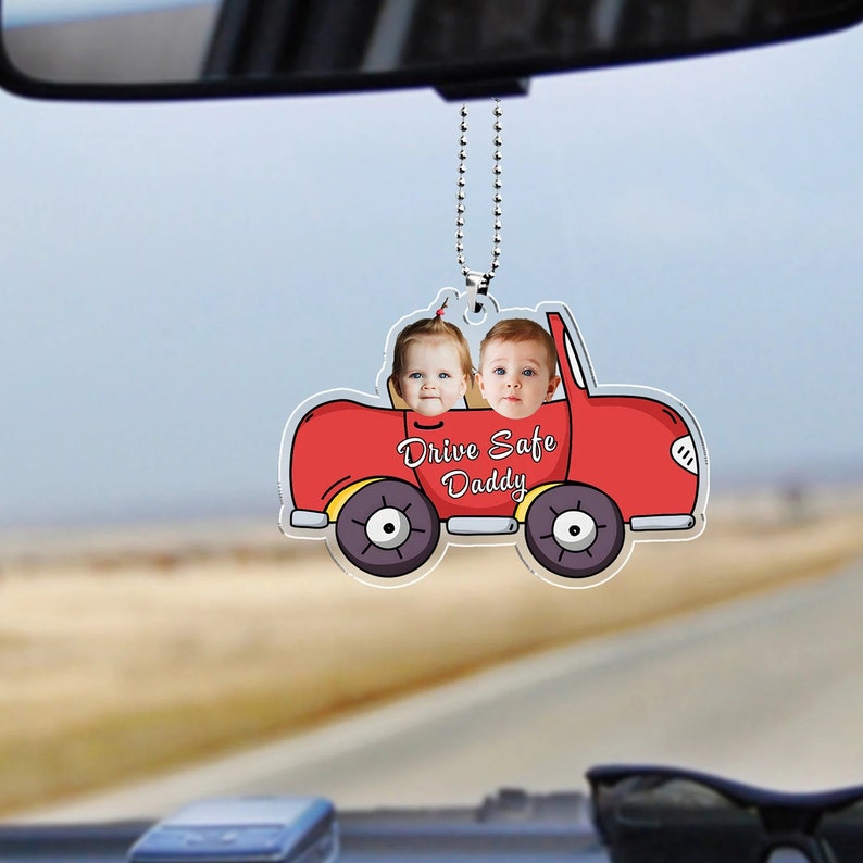 May include: Red car shaped rearview mirror charm with two children's faces in the windows. The car has yellow wheels and the text "Drive Safe Daddy" is printed on the car.
