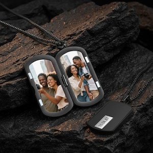 May include: Black rectangular locket necklace with a chain. The locket opens to reveal two photos. A smaller rectangular pendant with the date "10.08.87" is also visible. The locket and chain are on a dark, textured surface.