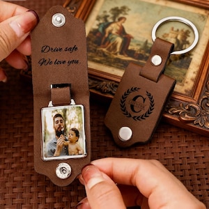 May include: Two brown leather keychains. One keychain has a photo and the text "Drive safe, We love you." The other keychain has the name "Chester" inside a wreath. Both keychains have silver hardware.