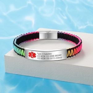 Puede incluir: Una pulsera de paracord de colores arcoíris con una etiqueta de alerta médica plateada. La etiqueta dice "Type 2 Diabetes, ICD MOM 123 6666 86548, ICD MOM 159 5872 25449".