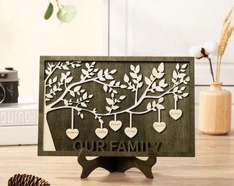 May include: A wooden family tree wall decor with a brown background and white cutout branches. The tree has seven hearts hanging from the branches, each with a name written on it: Jackson, Carter, Daniel, Avery, Lucille, and Selah. The text "OUR FAMILY" is written below the tree.