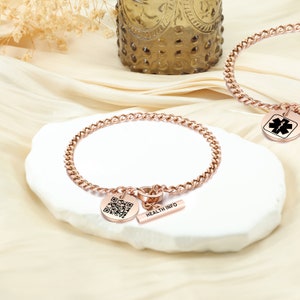 Könnte beinhalten: Rosenvergoldetes Kettenarmband mit einem runden Anhänger mit einem QR-Code und einem Barrenanhänger mit dem Text "HEALTH INFO".