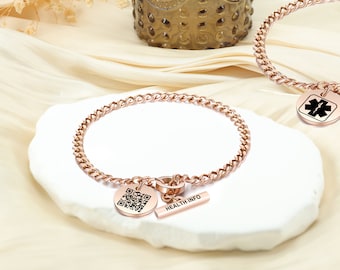 May include: Rose gold chain bracelet with a round charm featuring a QR code and a bar charm with the text "HEALTH INFO".