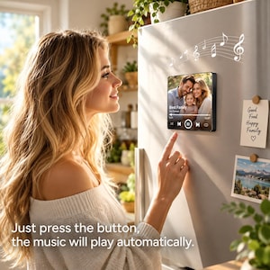 May include: A square digital display mounted on a refrigerator showing a family photo and music playback controls. Above the screen are white musical note graphics. Next to it are two paper notes with text and a landscape photograph.