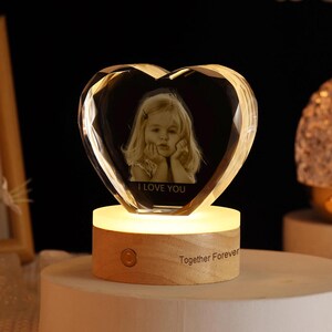 May include: A heart-shaped crystal with a photo of a young girl inside. The crystal is on a wooden base with a light and the words "I Love You" and "Together Forever" engraved on it.
