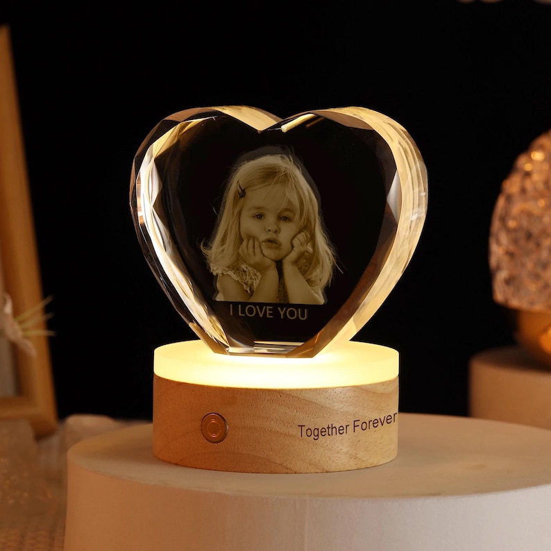 May include: A heart-shaped crystal with a photo of a young girl inside. The crystal is on a wooden base with a light and the words "I Love You" and "Together Forever" engraved on it.
