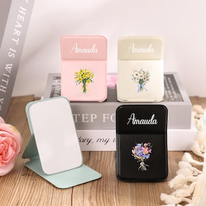 Op de afbeelding: Vier decoratieve cases met bloemmotieven. De cases zijn roze, crème en zwart, elk met de naam "Amauda" bovenaan gedrukt. Eén case heeft een boeket gele bloemen, een andere witte bloemen en de laatste een kleurrijk boeket.