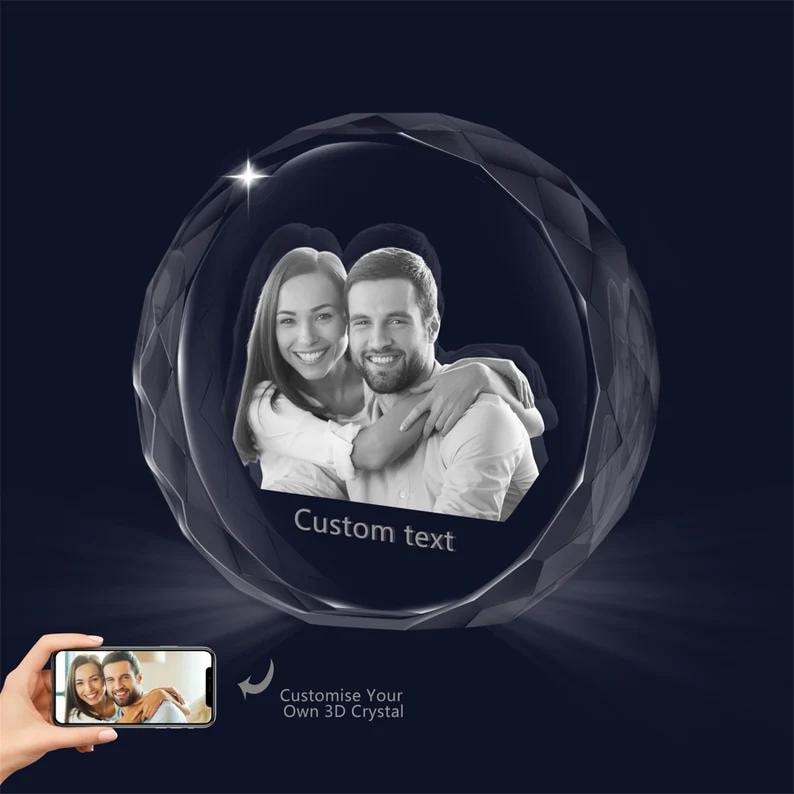 May include: A 3D crystal sphere with a photo of a couple inside. The sphere is clear and has a faceted design. The photo shows a man and a woman smiling and looking at each other. The text "Custom text" is printed on the sphere.