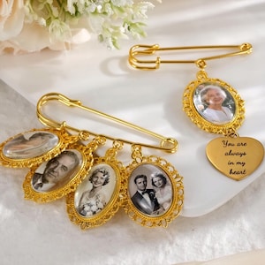 May include: Gold-coloured memorial pins with oval and heart-shaped pendants. The pendants display framed photographs of people. One pin has a heart-shaped pendant with the inscription "You are always in my heart."