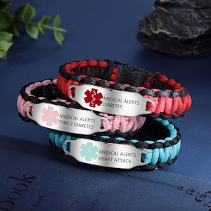 Op de afbeelding: Drie paracord armbanden met metalen medische waarschuwingslabels. De labels zijn zilverkleurig met een rood, roze en blauw medisch symbool. De tekst op de labels luidt "Medische waarschuwingen Type 2 Diabetes", "Medische waarschuwingen Diabetes" en "Medische waarschuwingen Hartaanval".